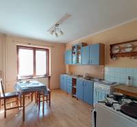 : Predaj rodinného domu s veľkým pozemkom v obci Pitelová  - Tradičná kuchyňa s modrou linkou, drevenou dekorom podlahy a jedálenským stolom.