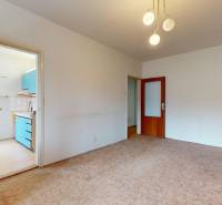 RADO I 2 IZBOVY BYT s loggiou I Adámiho ul. KARLOVA VES - Obývacia izba v 2-izbovom byte s kobercom a dreveným nábytkom, otvorené dvere do kuchyne.