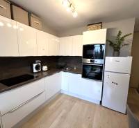 REZERVOVANÉ-PREDAJ 2 izbový byt s garážou v skvelej lokalite v Ružinov - Kuchyňa v 2-izbovom byte s bielymi skrinkami, spotrebičmi a podlahou s dreveným dekorom.