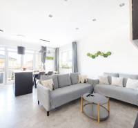 RADO I 3-izbový byt 84 m2 + terasa 13 m2 + parking I Veľký Biel- Senec - Obývacia izba v 3-izbovom byte s podlahou s dreveným dekorom a sivými sedačkami.