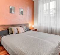  VÝNIMOČNÝ 4-izbový byt rozdelený na DVA SAMOSTATNÉ BYTY - Spálňa v 4-izbovom byte s podlahou s dreveným dekorom, oranžovou stenou a posteľou.