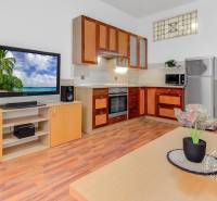  VÝNIMOČNÝ 4-izbový byt rozdelený na DVA SAMOSTATNÉ BYTY - Obývacia izba v 4-izbovom byte s kuchyňou, televízorom a podlahou s dreveným dekorom.