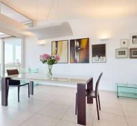 Exkluzívny byt pod Slavínom s terasou a výhľadom na Bratislavu - Jedáleň so stolom a stoličkami, veľké okná, obrazy na stene, kvetiny na stole.