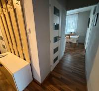 3 izbový byt bez balkóna Topoľčany  - Chodba v 3-izbovom byte s podlahou s dreveným dekorom a stolom pri okne.