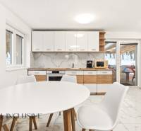 NADŠTANDARDNÁ REKREAČNÁ CHATA | DUCHONKA  - Kuchyňa v chate s bielym stolom, stoličkami a dreveným dekorom na skrinkách.