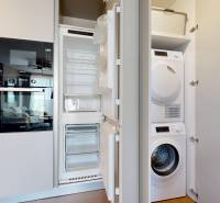 RIVERS | Butikovo zariadený ateliér na 32. poschodí Eurovea Tower - Kuchyňa v 2-izbovom byte so vstavanými spotrebičmi a práčkou na podlahe s dreveným dekorom.