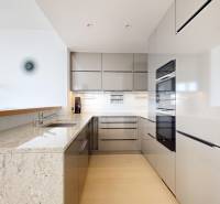 Elegantný byt na mieru s panorámou hradu  - Kuchyňa v 3-izbovom byte s lesklými skrinkami, mramorovou doskou a podlahou s dreveným dekorom.