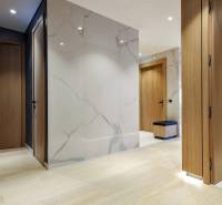 RIVERS I Prémiový 4-izbový byt s panoramatickým výhľadom na mesto - Chodba so stenou s mramorovým vzorom, drevenými dverami a podlahou s dreveným dekorom.