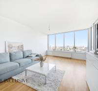 Na predaj luxusný 2-izb. byt s loggiou v Bratislave  - Obývacia izba s podlahou s dreveným dekorom, veľkými oknami a pohodlnou sedačkou v 2-izbovom byte.