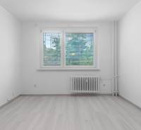 I Predaj 3- izbového bytu v Dúbravke - Izba v 3-izbovom byte s podlahou s dreveným dekorom a radiátorom pod oknom.