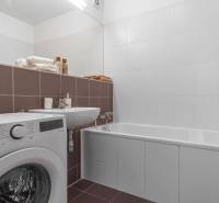 I na predaj 2i byt v komplexe Tri Veže na Bajkalskej - Kúpeľňa v 2-izbovom byte s práčkou, vaňou a umývadlom, vybavená bielymi a hnedými obkladmi.