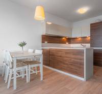 I na predaj 2i byt v komplexe Tri Veže na Bajkalskej - Kuchyňa v 2-izbovom byte s dreveným dekorom a bielym jedálenským stolom.