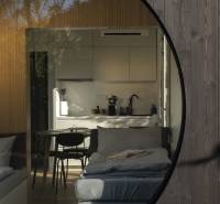 I Predaj Ecocapsule – autonómne ekologické bývanie - Interiér cez okrúhle okno, zvýrazňujúci Zvláštne nehnuteľnosti s kuchynským kútom a pohovkou.