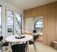 I Predaj Ecocapsule – autonómne ekologické bývanie - Interiér so stolom, stoličkami, podlahou s dreveným dekorom, výhľadom na rieku a kostol.
