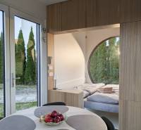 I Predaj Ecocapsule – autonómne ekologické bývanie - Interiér so stolom, ovocím a posteľou pri obloku, podlaha s dreveným dekorom.