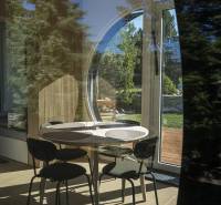 I Predaj Ecocapsule – autonómne ekologické bývanie - Interiér so stolom, stoličkami a podlahou s dreveným dekorom cez okno do záhrady.