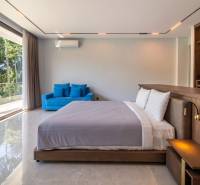 I Na predaj Luxusná vila „Tomma“ v Ubud, Bali - Spálňa s veľkými oknami, modrým gaučom a podlahou s dreveným dekorom vo vile.