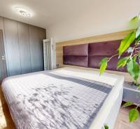 Na predaj nadštandardne zariadený 3 izb.byt, Trenčín, ul. Odevná - Spálňa v 3-izbovom byte s podlahou s dreveným dekorom, veľkou posteľou a rastlinou.