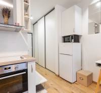 Prenájom 1-izbového bytu, Béžová, Béžová, Petržalka - REZERVOVANÉ - Kompaktná kuchyňa s varnou doskou, chladničkou a podlahou s dreveným dekorom v 1-izbovom byte.