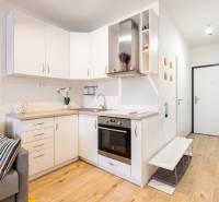 Prenájom 1-izbového bytu, Béžová, Béžová, Petržalka - REZERVOVANÉ - Kuchyňa s bielymi skrinkami v 1-izbovom byte a podlahou s dreveným dekorom.