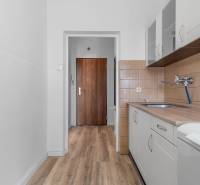 Komfortný 1,5-izbový byt s balkónom v Ružinove na predaj - Kuchyňa v 1-izbovom byte s podlahou s dreveným dekorom a bielou linkou.