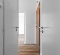 Komfortný 1,5-izbový byt s balkónom v Ružinove na predaj - Biely interiér 1-izbového bytu s podlahou s dreveným dekorom a otvorenými dverami.