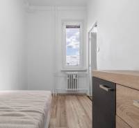 Komfortný 1,5-izbový byt s balkónom v Ružinove na predaj - Jednoduchá izba s posteľou, komodou a podlahou s dreveným dekorom v 1-izbovom byte.