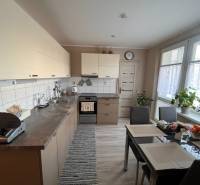 Na predaj  3-izbový byt v meste Rajec  - Kuchyňa v 3-izbovom byte so stolom, spotrebičmi a rastlinami.