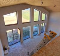 Únik z mesta, kde sa moderná architektúra stretáva s divokou prírodou? - Interiér chaty s veľkými oknami, schodíkmi a podlahou s dreveným dekorom.