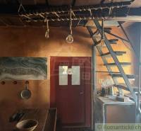 Štýlová chalupa v horskej dedinke Ratkovské Bystré - Interiér rodinného domu s drevenými schodmi, rustikálnym stolom a umeleckou maľbou na stene.