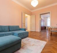 3-izbový byt s vysokými stropmi, Staré Mesto - Izba v 3-izbovom byte s modrou sedačkou, dreveným dekorom podlahy a jedálenským kútom.