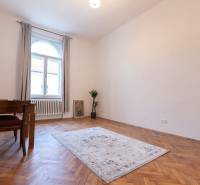3-izbový byt s vysokými stropmi, Staré Mesto - Izba v 3-izbovom byte s podlahou s dreveným dekorom, kobercom a stolom.