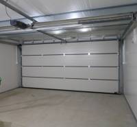 REZERVÁCIA _4-izb.rodinný dom na Okružnej ul.-Senec - Garáž s bielymi dverami, kosačka a náradie na ulici Okružná pri rodinnom dome.