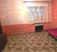 Rodinný dom v obci Pavlovce nad Uhom - Izba v rodinnom dome s kobercom, posteľou a skrinkou, záclonou na okne.