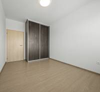 Svetlý 3-izbový byt 90 m² s terasou 18,5 m², 2 garáže, Smaragdová ul. - Izba v 3-izbovom byte so skriňou a podlahou s dreveným dekorom.