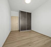 Svetlý 3-izbový byt 90 m² s terasou 18,5 m², 2 garáže, Smaragdová ul. - Izba v 3-izbovom byte s bielymi stenami a podlahou s dreveným dekorom.