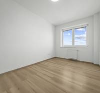 Svetlý 3-izbový byt 90 m² s terasou 18,5 m², 2 garáže, Smaragdová ul. - Prázdna izba s oknom, bielymi stenami a podlahou s dreveným dekorom.