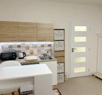 Kompletne zrekonštruovaná garzónka na prenájom, Internátna ulica - Garsónka so svetlou kuchynskou linkou, bielym barovým pultom a podlahou s dreveným dekorom.