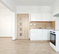 | 2-izbový byt + parking, ul. Východná | Trenčín - Kuchyňa v 2-izbovom byte s bielymi skrinkami, sporákom a podlahou s dreveným dekorom.