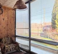 Rodinný dom s veľkou terasou a garážou v  Lastovciach za  73 500 € - Rodinný dom s ratanovou lampou, kreslom s dekou a oknami so žalúziami.