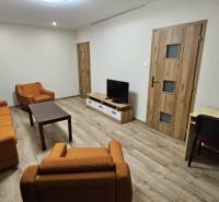 Prenájom 2 izbový byt v Topoľčanoch, sídlisko JUH - Obývacia izba v 2-izbovom byte s oranžovým nábytkom a podlahou s dreveným dekorom.
