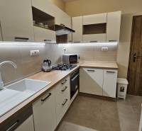 Prenájom 2 izbový byt v Topoľčanoch, sídlisko JUH - Kuchyňa v 2-izbovom byte s bielymi skrinkami a podlahou s dreveným dekorom.