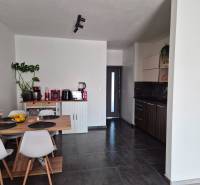 3-izb. byt v obci Blatná na Ostrove, balkón, lodžia, novostavba - Kuchyňa v 3-izbovom byte s jedálenským stolom, tmavá podlaha a biele stoličky.