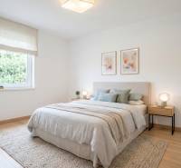 NOVINKA - 2x Novostavba RODINNÝCH DOMOV - Borčice  - Svetlá spálňa s podlahou s dreveným dekorom, posteľ so svetlým prehozom a obrazmi na stene.