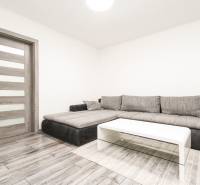 3i byt 73m2 + 6m2 balkón, Gen. Svobodu, Trenčín - Svetlá obývačka v 3-izbovom byte s rohovou sedačkou a podlahou s dreveným dekorom.