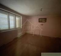 Rodinný dom v pôvodnom stave na 7 árovom pozemku v Tvrdošovciach - Prázdna izba v rodinnom dome s podlahou s dreveným dekorom a veľkým oknom.