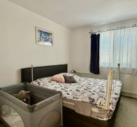 * 7i rodinný dom, veľký 33.5á pozemok, Brestovany - Spálňa v rodinnom dome s posteľou, detskou postieľkou a oknom s tmavými závesmi.