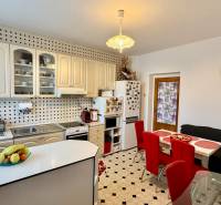 * 7i rodinný dom, veľký 33.5á pozemok, Brestovany - Kuchyňa v rodinnom dome s bielymi skrinkami, jedálenským stolom a červenými stoličkami.