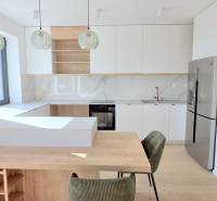 LUXUSNÝ 3i byt,PARKING,CHLADENIE,TERASA,Grand Koliba, Frankovská ulica - Kuchyňa v 3-izbovom byte s drevenými a bielymi prvkami a závesnými lampami.