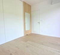 LUXUSNÝ 3i byt,PARKING,CHLADENIE,TERASA,Grand Koliba, Frankovská ulica - Izba v 3-izbovom byte s drevenou podlahou, vstavanou skriňou a bielymi stenami.